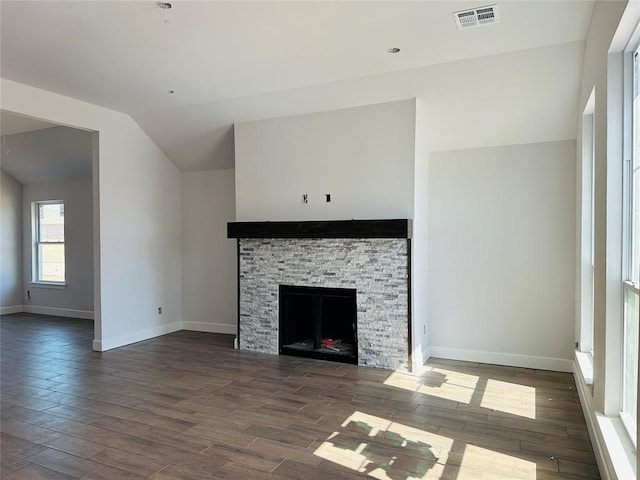 unfurnished living room featuring visible vents, lofted ceiling, dark wood-type flooring, and a stone fireplace