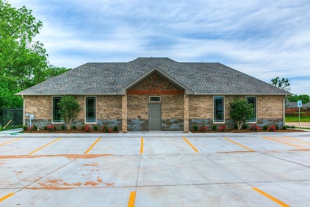 view of front facade featuring brick siding, roof with shingles, and uncovered parking