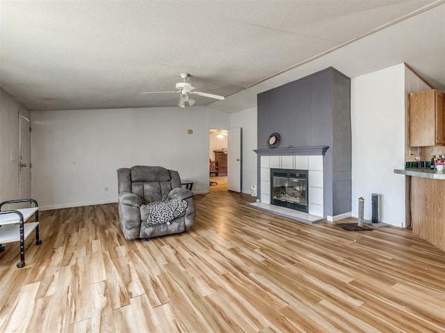 living room with ceiling fan, light hardwood / wood-style floors, and a tile fireplace