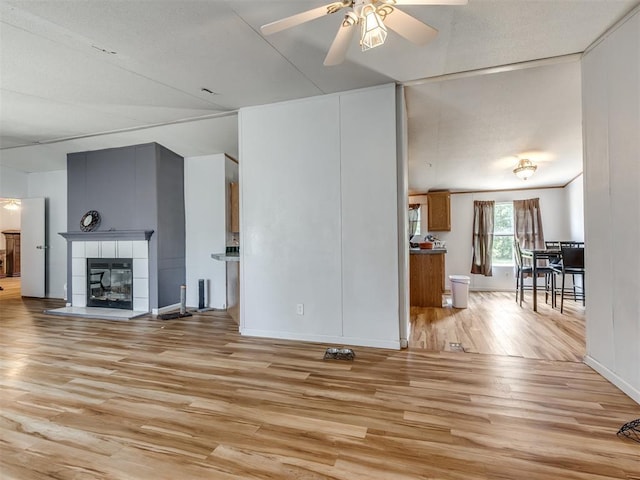 unfurnished living room featuring ceiling fan, a textured ceiling, a tile fireplace, and light hardwood / wood-style flooring