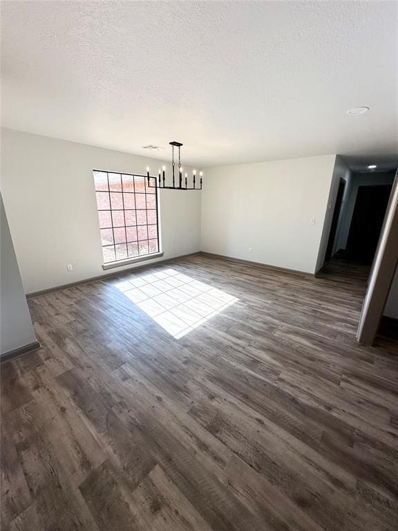 unfurnished dining area with dark wood-type flooring, a textured ceiling, and an inviting chandelier