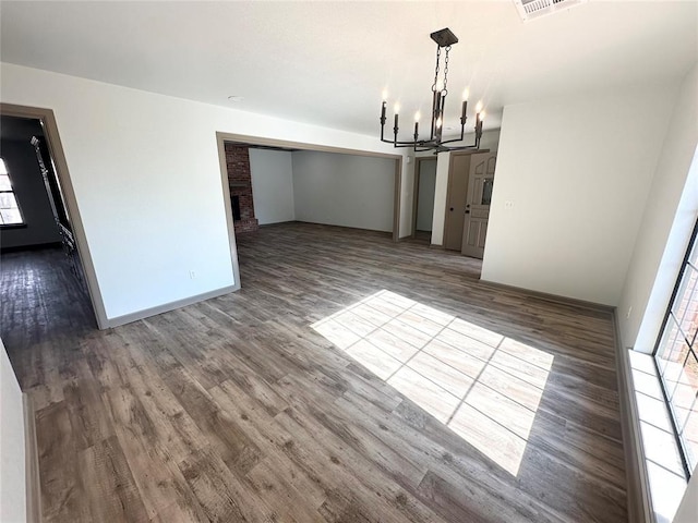 unfurnished dining area featuring hardwood / wood-style floors, a brick fireplace, and a notable chandelier