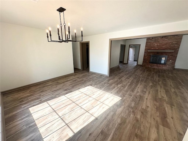 unfurnished dining area featuring hardwood / wood-style flooring, a brick fireplace, and a chandelier