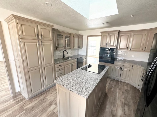 kitchen with backsplash, a skylight, light hardwood / wood-style flooring, and black appliances