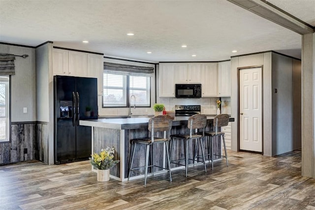 kitchen featuring wood-type flooring, a center island, white cabinetry, and black appliances