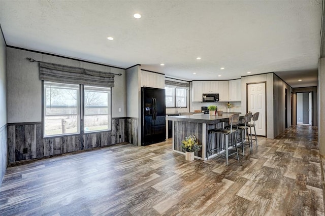 kitchen featuring a center island, black appliances, white cabinets, wood-type flooring, and a breakfast bar area