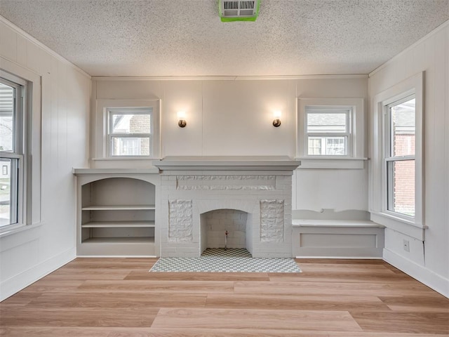 unfurnished living room with a textured ceiling, plenty of natural light, a fireplace, and light hardwood / wood-style flooring