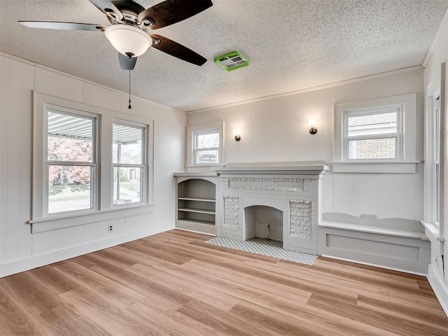 unfurnished living room with light hardwood / wood-style floors, a brick fireplace, and a healthy amount of sunlight