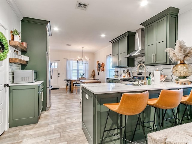 kitchen with kitchen peninsula, green cabinets, and wall chimney range hood