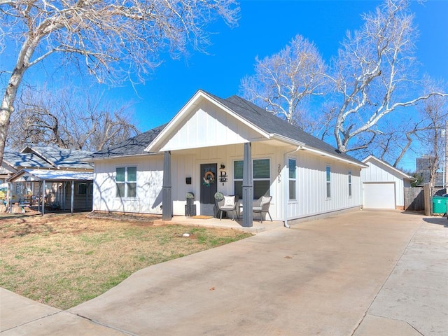 view of front of house with covered porch, an outdoor structure, driveway, a front lawn, and board and batten siding