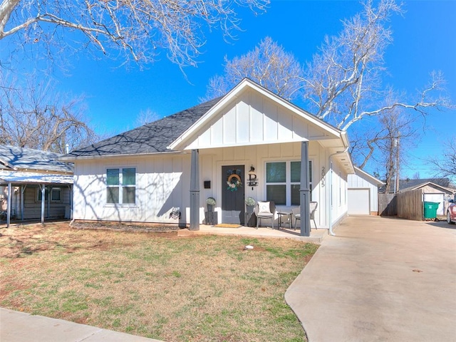 view of front facade featuring an outbuilding, covered porch, board and batten siding, a front yard, and a garage