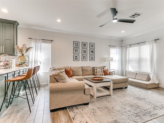 living area featuring ornamental molding, light wood-type flooring, visible vents, and baseboards