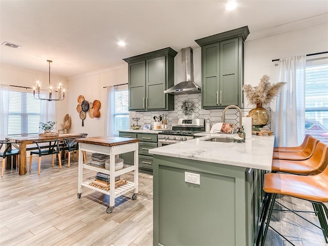 kitchen featuring wall chimney range hood, ornamental molding, green cabinets, and stainless steel range with gas stovetop