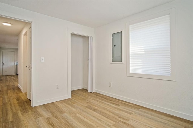 unfurnished bedroom with light hardwood / wood-style floors, electric panel, and a closet