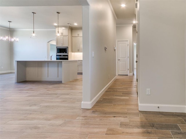 kitchen with light wood finished floors, arched walkways, ornamental molding, wall oven, and stainless steel microwave