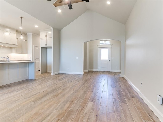 unfurnished living room featuring light wood finished floors, baseboards, arched walkways, a ceiling fan, and a sink