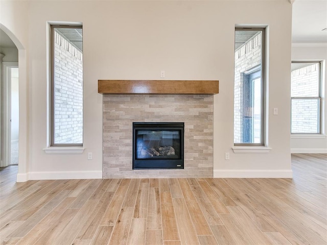 unfurnished living room featuring baseboards, wood finished floors, ornamental molding, and a tile fireplace