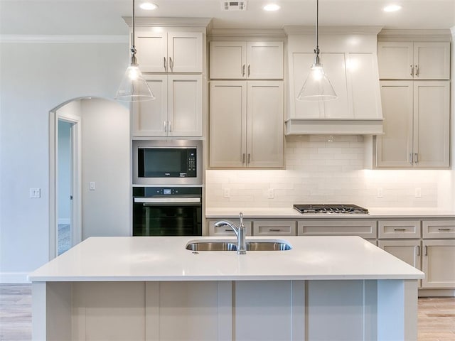 kitchen featuring crown molding, decorative backsplash, appliances with stainless steel finishes, light wood-style floors, and arched walkways