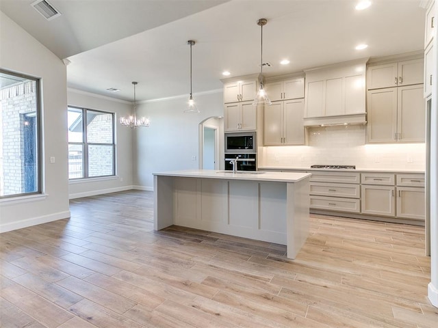 kitchen with light wood-style flooring, arched walkways, light countertops, appliances with stainless steel finishes, and tasteful backsplash