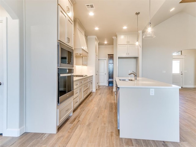 kitchen featuring visible vents, custom range hood, a sink, appliances with stainless steel finishes, and light wood finished floors