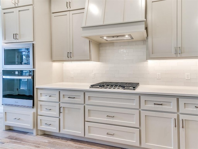 kitchen with decorative backsplash, custom exhaust hood, light countertops, and stainless steel appliances