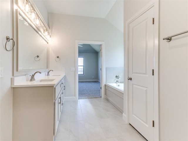 bathroom with double vanity, a garden tub, lofted ceiling, and a sink