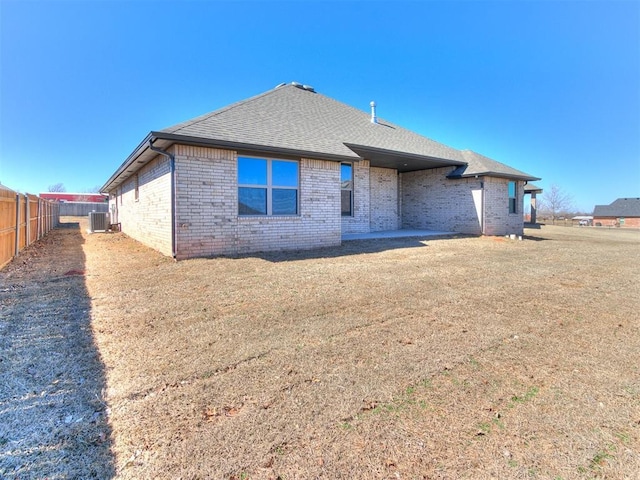 rear view of house with a lawn, central AC, fence, roof with shingles, and brick siding