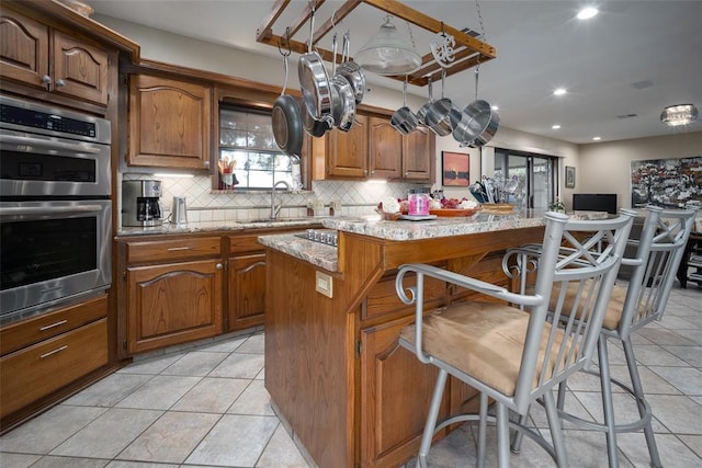 kitchen featuring light stone countertops, sink, stainless steel double oven, a kitchen bar, and a kitchen island