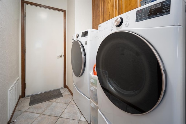 washroom with washing machine and clothes dryer, light tile patterned flooring, and cabinets