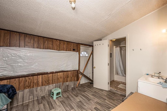 bedroom with sink, wooden walls, vaulted ceiling, hardwood / wood-style flooring, and a textured ceiling