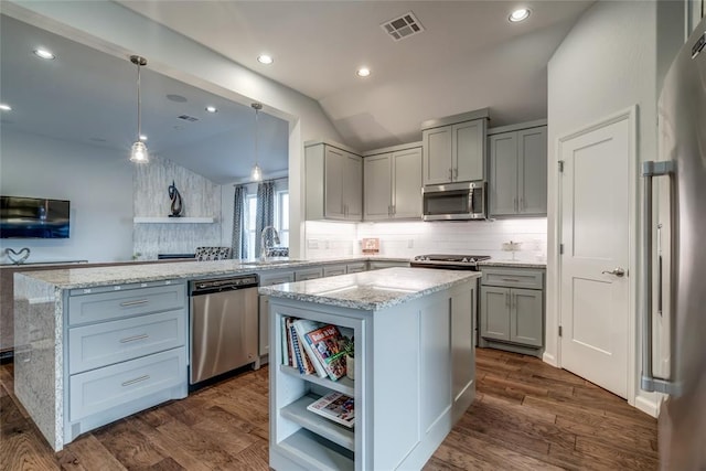 kitchen with kitchen peninsula, appliances with stainless steel finishes, dark hardwood / wood-style flooring, a kitchen island, and lofted ceiling