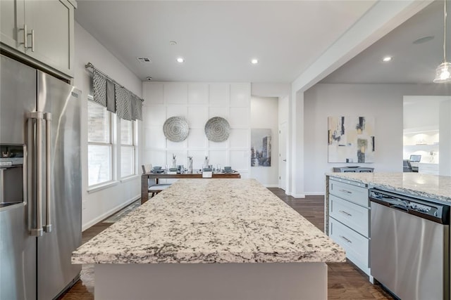 kitchen with appliances with stainless steel finishes, dark hardwood / wood-style floors, a kitchen island, and light stone counters