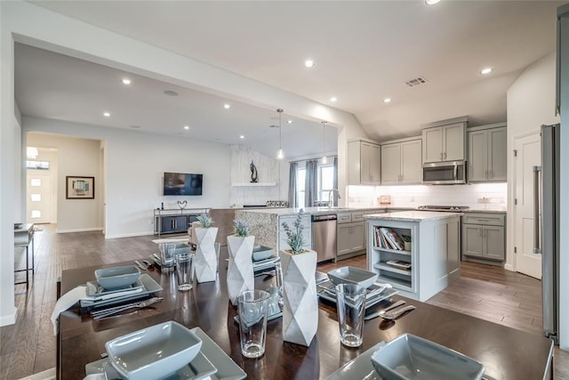 kitchen with a center island, dark wood-type flooring, decorative light fixtures, vaulted ceiling, and appliances with stainless steel finishes