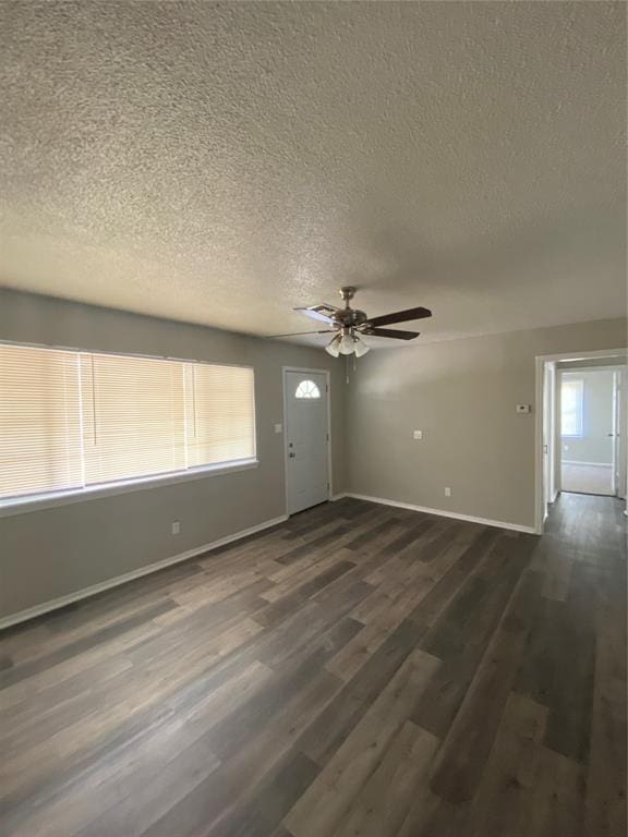 unfurnished living room featuring ceiling fan, plenty of natural light, dark wood-type flooring, and a textured ceiling