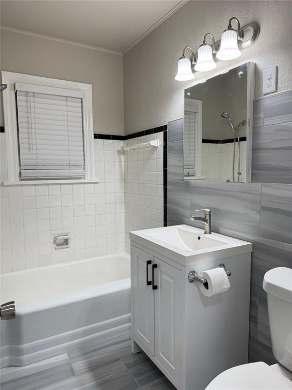 full bathroom with vanity, tub / shower combination, toilet, and tile walls