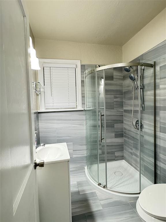 bathroom with an enclosed shower, vanity, tile walls, tile patterned flooring, and toilet