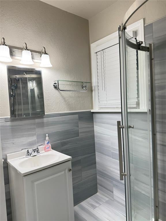 bathroom with vanity, a shower with shower door, and tile walls