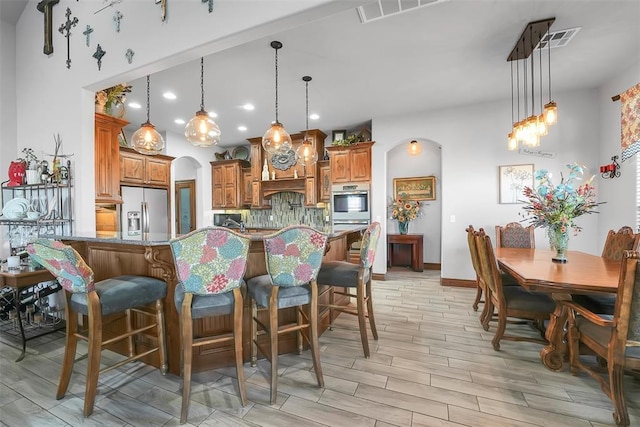 kitchen with a kitchen bar, appliances with stainless steel finishes, decorative light fixtures, and light stone counters