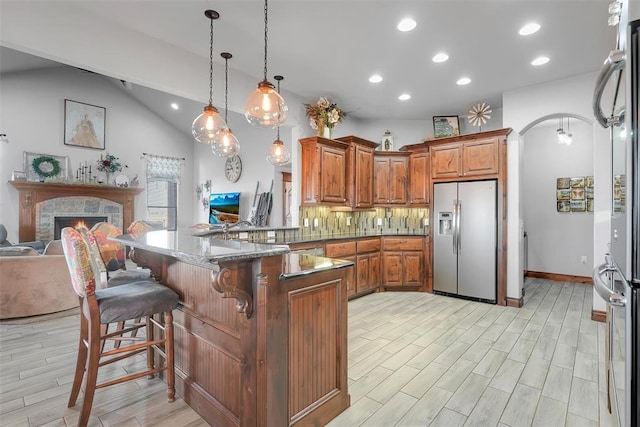 kitchen with pendant lighting, a breakfast bar, backsplash, stainless steel fridge, and kitchen peninsula