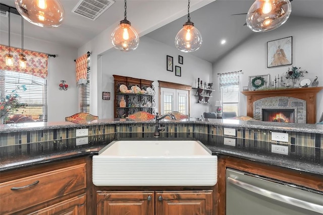 kitchen featuring dishwasher, a stone fireplace, sink, hanging light fixtures, and vaulted ceiling