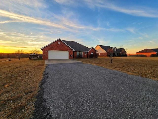 ranch-style house with an attached garage, gravel driveway, brick siding, and a yard