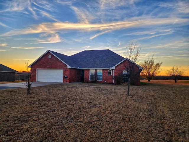 ranch-style home featuring roof with shingles, driveway, a lawn, brick siding, and a garage
