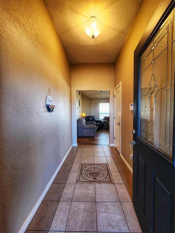 hall with a textured wall, tile patterned flooring, and baseboards