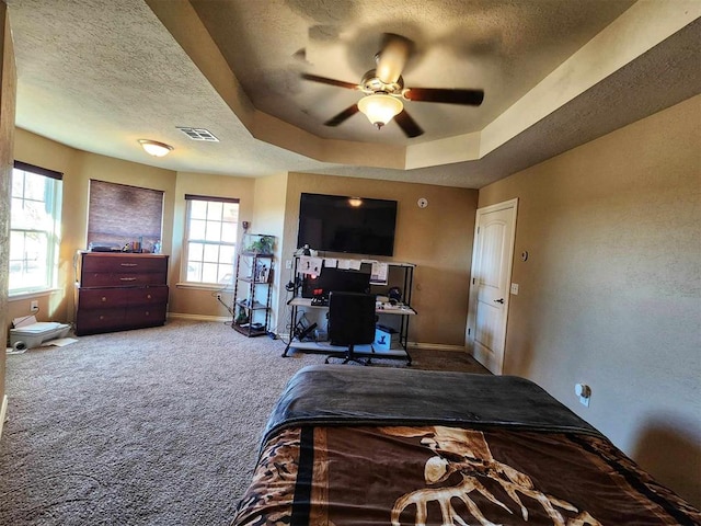carpeted bedroom featuring baseboards, visible vents, a textured ceiling, and a tray ceiling