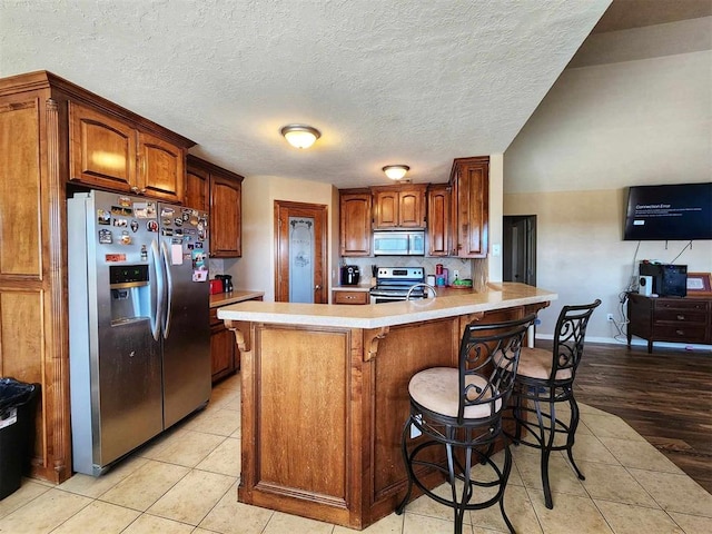 kitchen with a breakfast bar, light tile patterned floors, light countertops, a peninsula, and appliances with stainless steel finishes