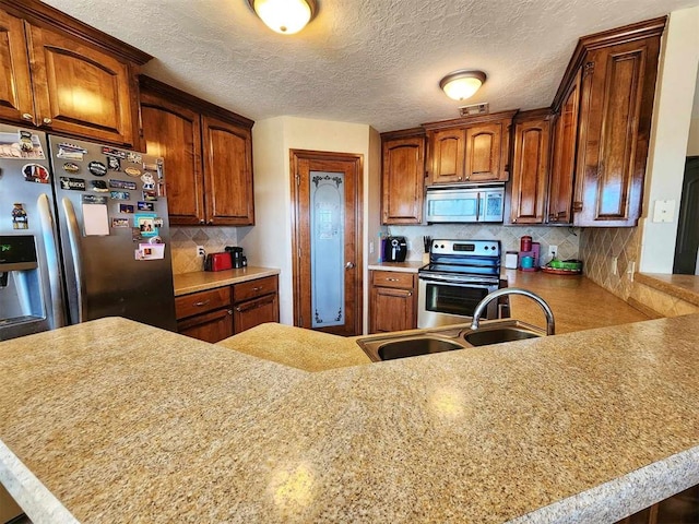 kitchen with stainless steel appliances, backsplash, light countertops, a sink, and a peninsula