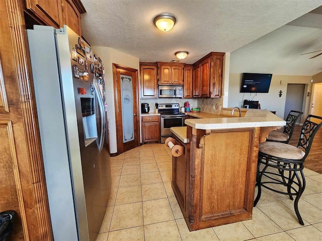 kitchen with light tile patterned floors, a breakfast bar area, light countertops, a peninsula, and appliances with stainless steel finishes