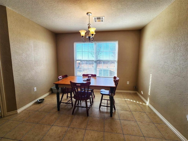 tiled dining area with a textured wall, a chandelier, a textured ceiling, and visible vents