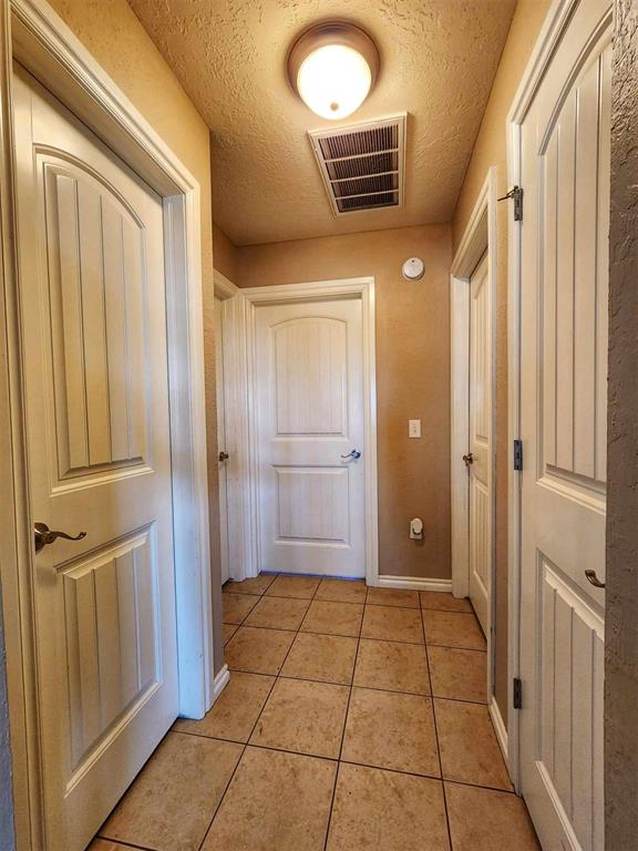 hallway with light tile patterned flooring, a textured ceiling, visible vents, and baseboards