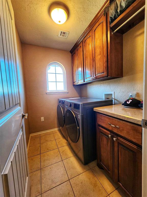 washroom featuring washing machine and clothes dryer, a textured ceiling, light tile patterned flooring, cabinet space, and visible vents
